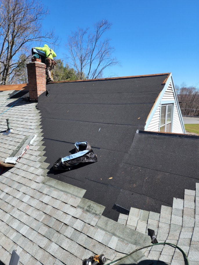 A dark shingle roof being finished near a chimney